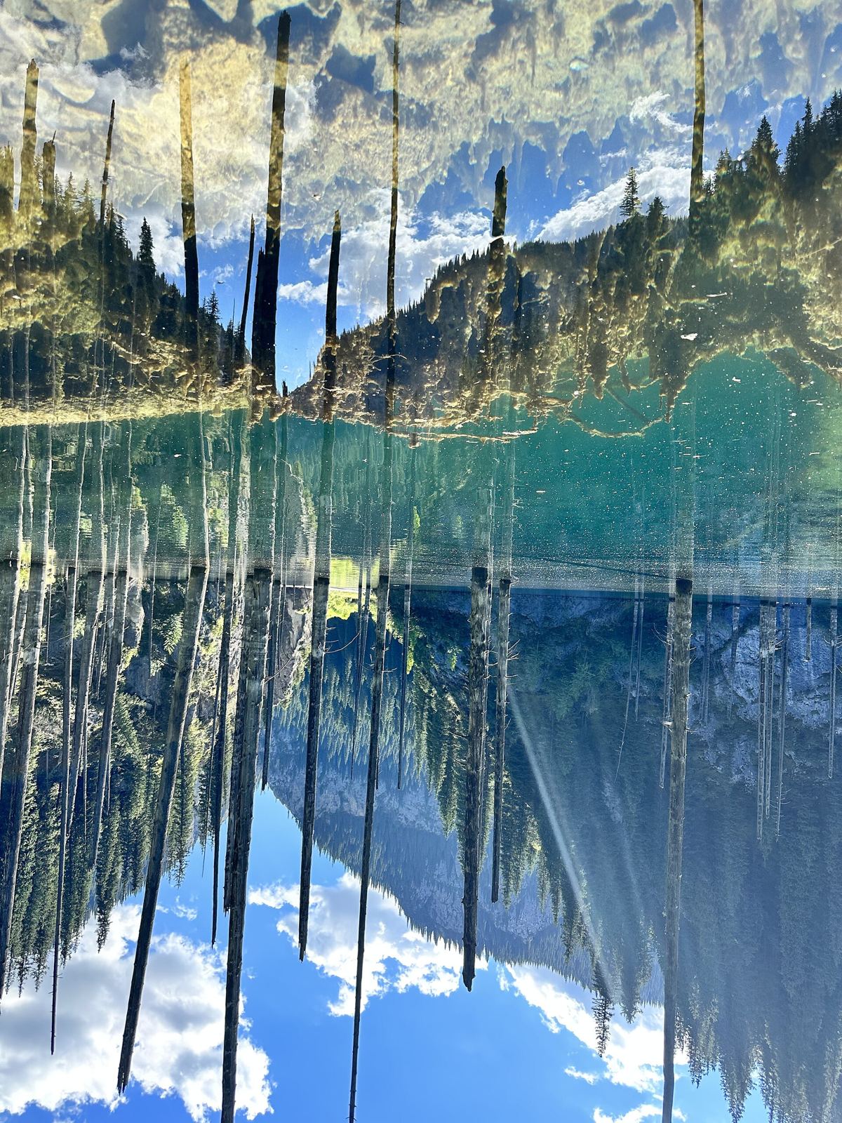 Mirror reflection of the sunken forest in calm Lake Kaindy water